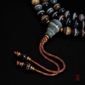 Detailed view of SHADOWED TIDES tapered focal bead and multicolored braided tassel