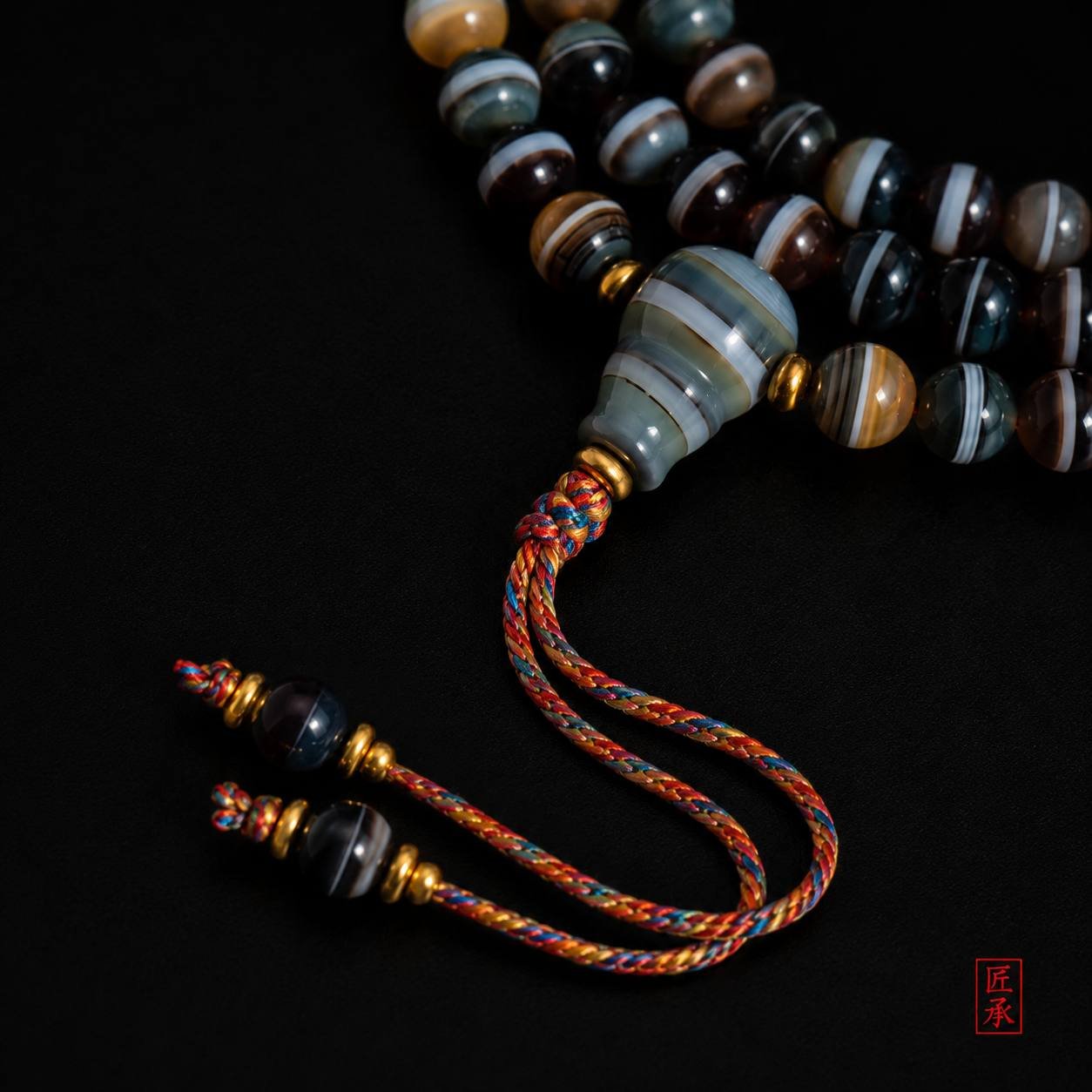 Detailed view of SHADOWED TIDES tapered focal bead and multicolored braided tassel