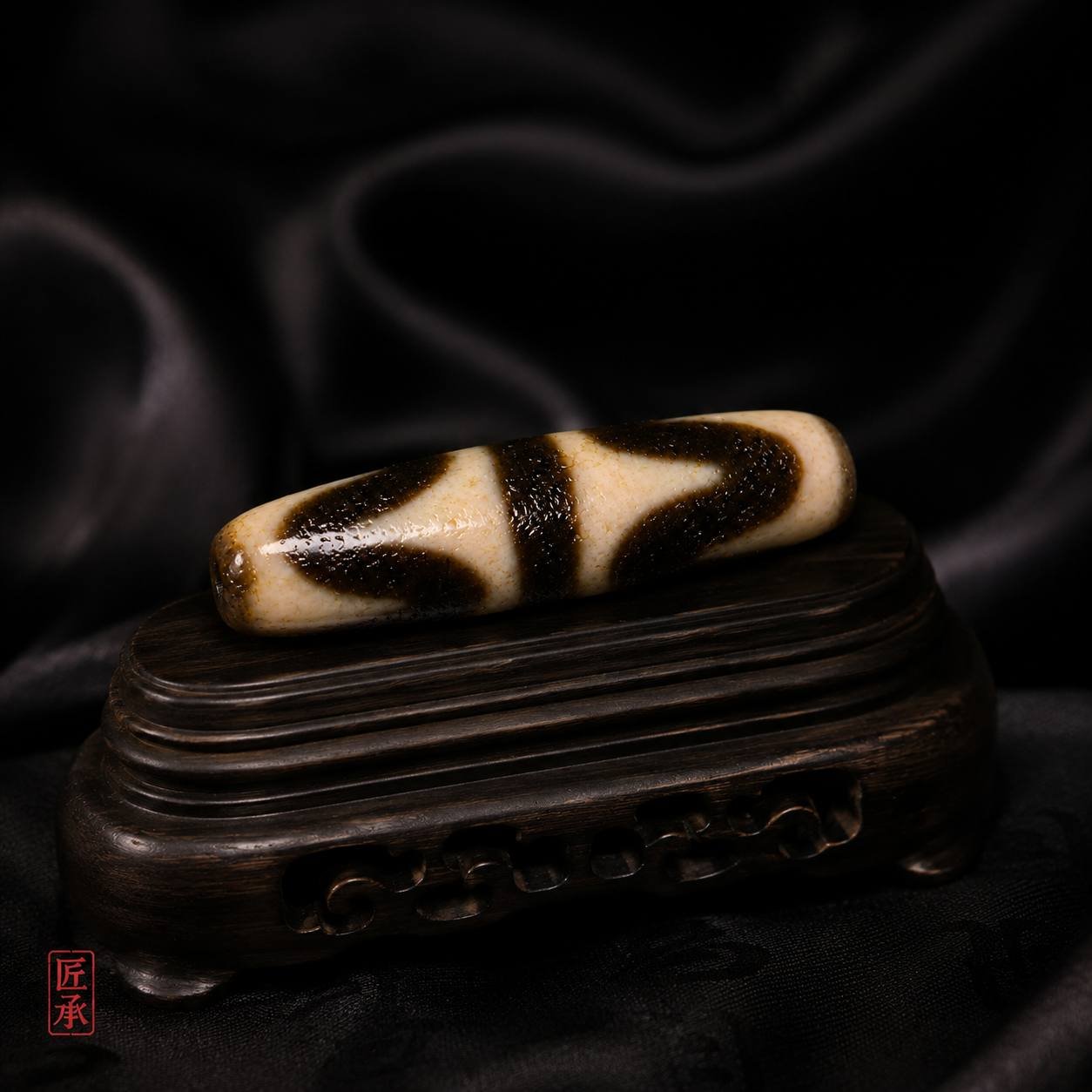 Tiger Tooth Dzi bead displayed on a carved wooden stand